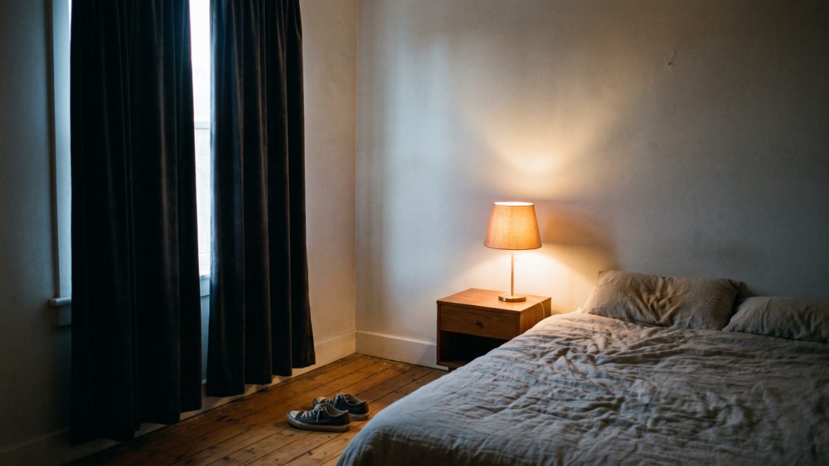 Leeres Schlafzimmer im Morgengrauen, zerknitterte Bettwäsche und ein Paar Trainingsschuhe neben dem Bett.